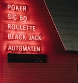 Red neon letters are mounted on a dark tiled wall, displaying the words Poker, Sic Bo, Roulette, Black Jack, and Automaten.