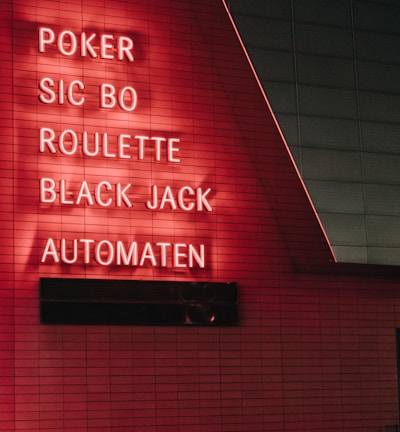 Red neon letters are mounted on a dark tiled wall, displaying the words Poker, Sic Bo, Roulette, Black Jack, and Automaten.