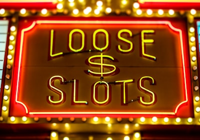 Bright neon lights display the words 'Loose Slots' with a dollar sign in the center. The sign is outlined with bulbs, creating a vibrant and flashy effect typical of a casino or entertainment venue.