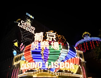 Bright neon signs in multiple colors illuminate the night, prominently displaying the name 'Casino Lisboa' alongside signage in Chinese characters. The lights form intricate patterns and vibrant displays, creating a lively and energetic atmosphere.