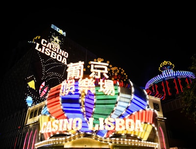 Bright neon signs in multiple colors illuminate the night, prominently displaying the name 'Casino Lisboa' alongside signage in Chinese characters. The lights form intricate patterns and vibrant displays, creating a lively and energetic atmosphere.