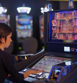 A person is seated at a slot machine console in a casino, focusing intently on the game displayed on the screen. The background shows several other illuminated gaming machines, adding a vibrant and colorful atmosphere to the scene.