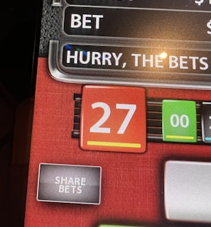 A digital display screen showing a casino betting interface, with text prompting to hurry bets and a highlighted number 27 in red. There are options for betting amounts and a 'share bets' button.