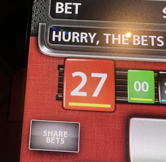 A digital display screen showing a casino betting interface, with text prompting to hurry bets and a highlighted number 27 in red. There are options for betting amounts and a 'share bets' button.
