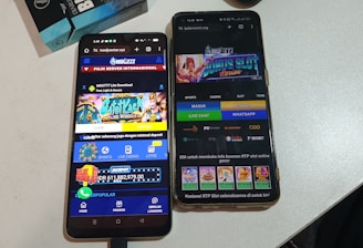 Two smartphones are displayed on a white surface, both showing gambling websites with colorful graphics, text, and various options for logging in and accessing games. The screens are bright and filled with promotional content related to casino and slot games.
